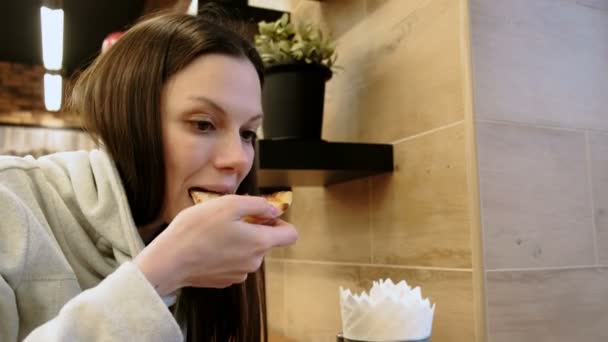 Brunette jonge hongerige vrouw bijt uit een lekkere plak van pizza en kauwt het, zijaanzicht. — Stockvideo