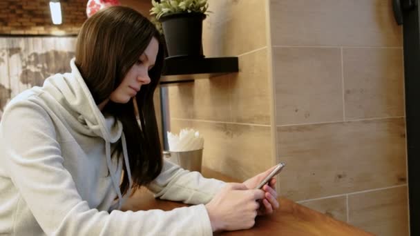 Mujer morena joven pensativa en una camisa brillante lee el mensaje en su teléfono celular sentado en la cafetería . — Vídeos de Stock