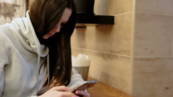 Zamyślony młoda brunetka Kobieta w jasnej koszuli w jej telefon komórkowy siedząc w kawiarni. — Wideo stockowe