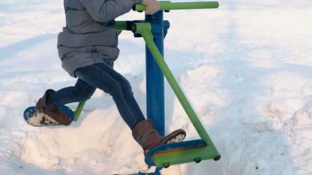 Κοντινό πλάνο Γυναίκα πόδια κάνει ασκήσεις ποδιών σε προσομοιωτή σε ένα χειμερινό πάρκο στην πόλη. Πλάγια όψη. — Αρχείο Βίντεο