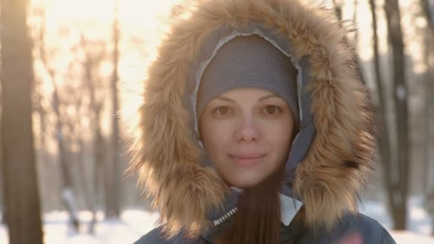 Close-up Frauengesicht mit Fellkapuze blickt in die Kamera und lächelt im wintersonnigen Park. — Stockvideo