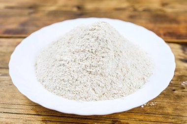 Buğday unu kaba ahşap arka plan üzerinde beyaz plaka ile yakın çekim yığın fotoğraf Üstten bakış yaptı