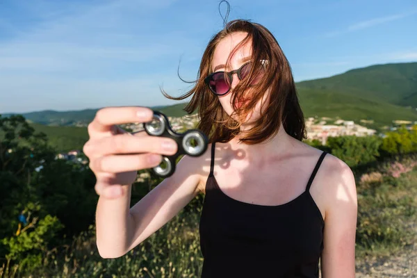 Chica joven se para en una montaña, sostiene un hilandero en su mano y lo mira. vista frontal . — Foto de Stock