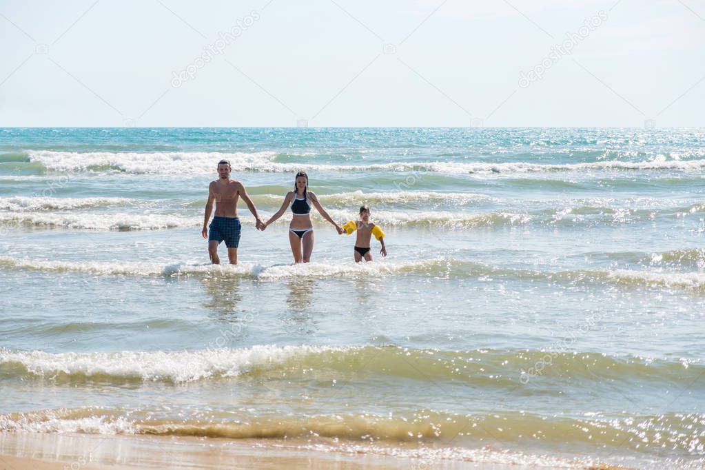 Dad, mom and son come out of the sea after swimming. Bif storm waves. Boy iin water wings.
