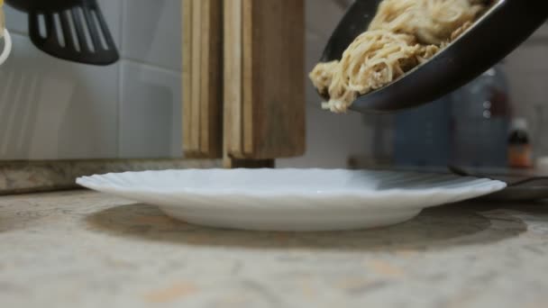Primer plano de poner la pasta terminada con una pala de madera de la sartén en un plato sobre la mesa . — Vídeos de Stock