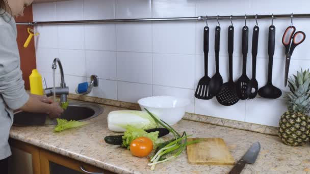 Woman brunette washes lettice for salad in the kitchen. Side view. — Stock Video