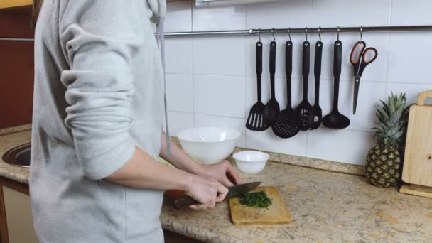 Une femme méconnaissable coupe de l'aneth sur une planche à découper sur une table de cuisine. Mains en l'air . — Video