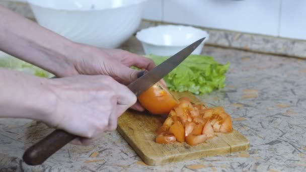 Unrecognizable woman cut tomato into small pieces on cutting board on kitchen table. Hands close up. — Stock Video