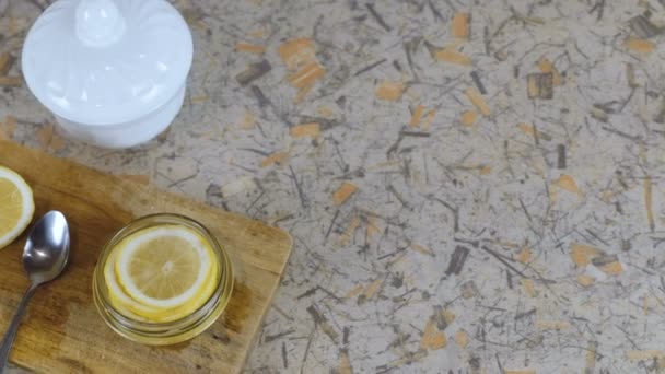 Close-up lemon slices in jar, spoon, half lemon, sugar bowl on cutting board and kitchen table. — Stock Video