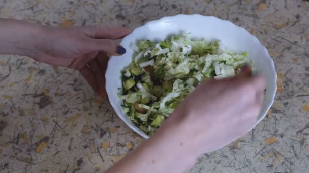 Eine unkenntliche Frau mischt Gemüsesalat auf einem weißen Teller auf dem Küchentisch. Hände aus nächster Nähe. — Stockvideo