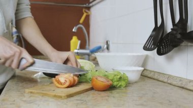 Tanınmayan kadın mutfakta bir kesme tahtası domates keser. Eller yakın çekim.