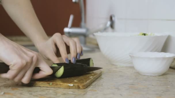 Close-up de mãos de mulher cortando pepino na placa de corte na mesa da cozinha. Vista lateral . — Vídeo de Stock