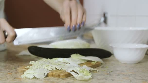 Primer plano de las manos de la mujer cortan la col china en la tabla de cortar en la mesa de la cocina. Cuchillo golpeador . — Vídeos de Stock