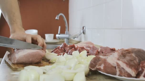 Hände in Großaufnahme schneiden ein großes Stück Schweinefleisch in kleine Stücke für Schweinekoteletts. Seitenansicht. — Stockvideo