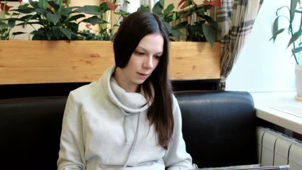 Morena jovem mulher em uma jaqueta leve lê e vira através do menu sentado em um café. Close-up . — Vídeo de Stock