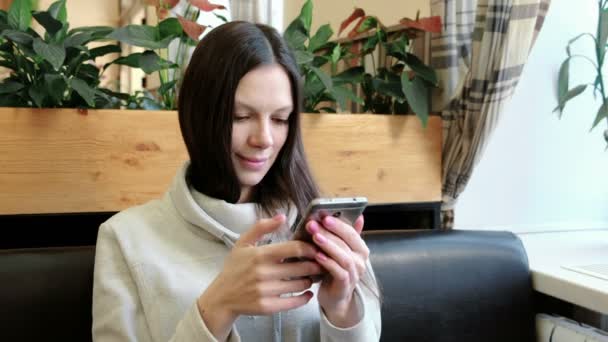 Piękna kobieta brunetka czatować na jej telefon w kawiarni i uśmiechając się. — Wideo stockowe