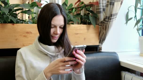 Mooie brunette vrouw gebruikt voor web haar mobiel in café en glimlachen. — Stockvideo