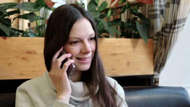 Belle femme brune parlant son téléphone portable dans un café et souriant . — Video