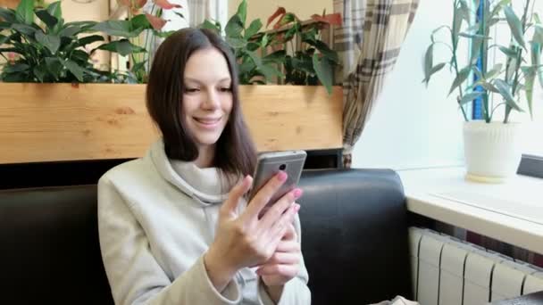 Hermosa mujer morena hablando videochat por su teléfono celular en la cafetería y sonriendo . — Vídeo de stock