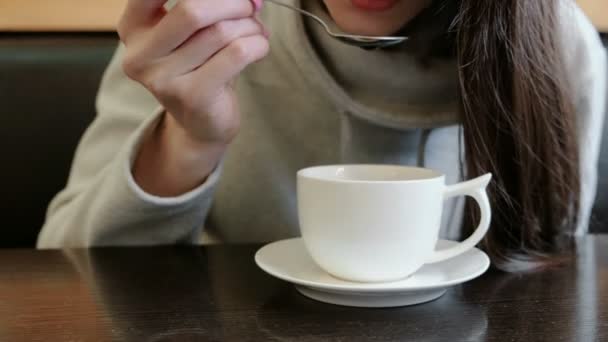 Unrecognizable woman drinks hot tea from cup with a spoon. Close up hands and mouth. — Stock Video