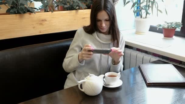 Девушка брюнетка фотографии чайник и Кубок в кафе на мобильный телефон. Вид спереди . — стоковое видео