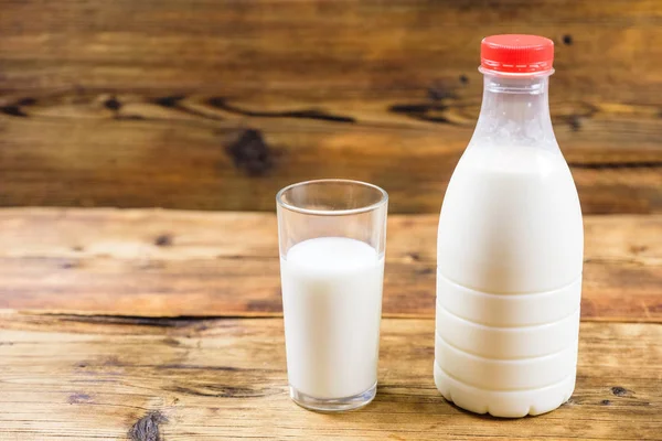 Bottle of fresh farm milk with red lid and glass of milk on wooden background. Side view.