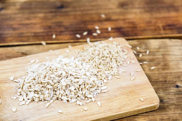 Close-up oat flakes and grain oats in a wooden board. Farm-fresh product. Side view. — Stock Photo, Image