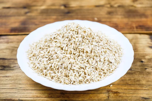 Close-up dry oat flakes in white plate in a wood background. Farm-fresh product. Top view. — Stock Photo, Image