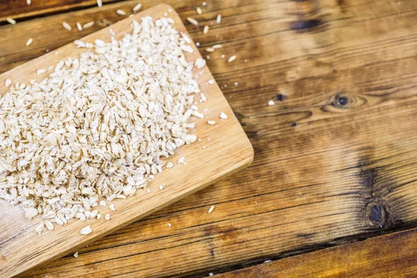 Close-up bunch farm oat flakes in a wooden board. Farm-fresh product. Top view. — Stock Photo, Image