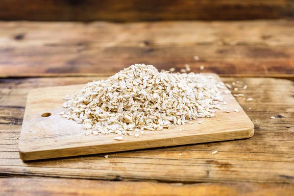 Close-up bunch farm oat flakes in a wooden board. Farm-fresh product. Side view. — Stock Photo, Image