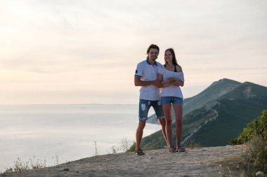 Erkek ve kadın deniz manzarası ile bir dağ yolundan günbatımı ve kamera bakmak tutuyoruz. Önden Görünüm.