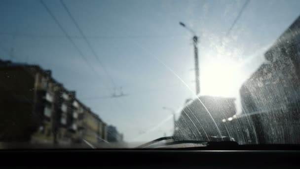 Vista desde el coche a la ciudad. Concéntrate en el sucio parabrisas. El coche está en movimiento. . — Vídeos de Stock