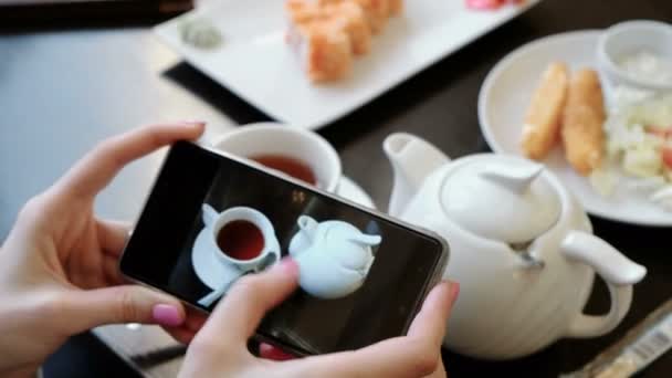Bardak çay ve çaydanlık cep telefonunun ekranında fotoğraflar aracılığıyla leafing kadının elleri. — Stok video