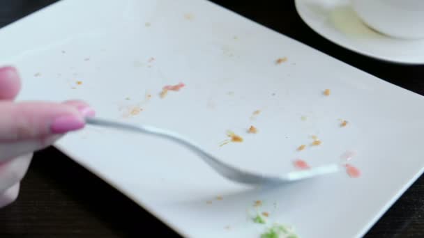 Γυναικείο χέρι γκρο πλαν συλλέγει τα υπολείμματα του φαγητού με ένα λευκό ορθογώνιο πιάτο με ένα πιρούνι. — Αρχείο Βίντεο