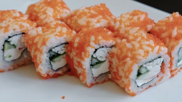 Close-up acht rolt met kaviaar met ingelegde gember en wasabi op een witte rechthoekige plaat. — Stockvideo