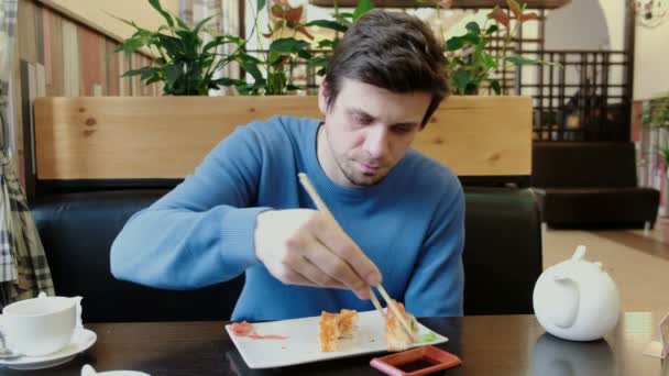 Ο νεαρός άνδρας μελαχρινή ντιπ ρολό σε σάλτσα σόγιας από ξύλο μπαστούνια και το τρώει. Μπροστινή όψη. — Αρχείο Βίντεο