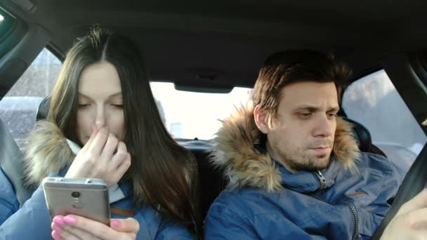 Homme et femme brune en bleus doudounes regarder quelque chose dans leurs téléphones cellulaires assis dans la voiture . — Video