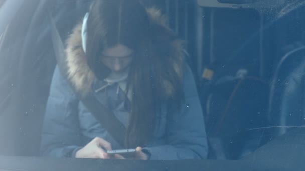 Vue à travers le pare-brise de la voiture sur la jeune femme brune en duvet bleu regardant le téléphone . — Video