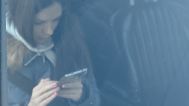 Blick durch die Windschutzscheibe des Autos auf eine Frau, die auf das Telefon schaut. Frontscheibe im Fokus. — Stockvideo