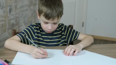 Basit bir kalem masada oturan ile oval çizgili tişört içinde yedi yaşında çocuk çizer.