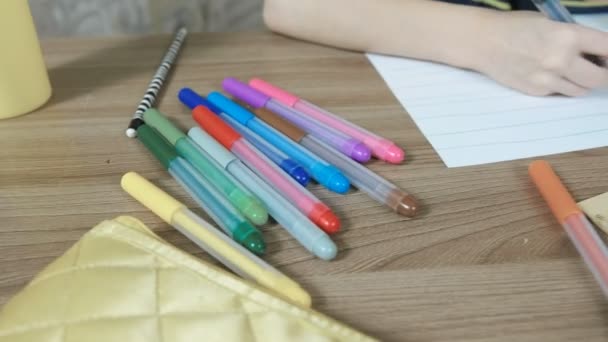 Niño de 7 años está pintando su pintura con lápiz de fieltro azul en papel rayado sentado junto a la mesa . — Vídeos de Stock