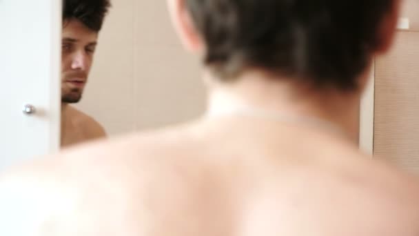 Ospalý muž při pohledu do zrcadla. Unavený muž, který se právě probudil se připravuje pro své ranní sprchu — Stock video