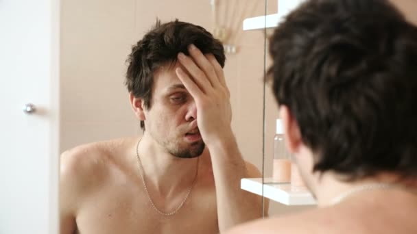 Hombre cansado que acaba de despertarse mirando su reflejo en el espejo y se frota la cara con la mano . — Vídeo de stock