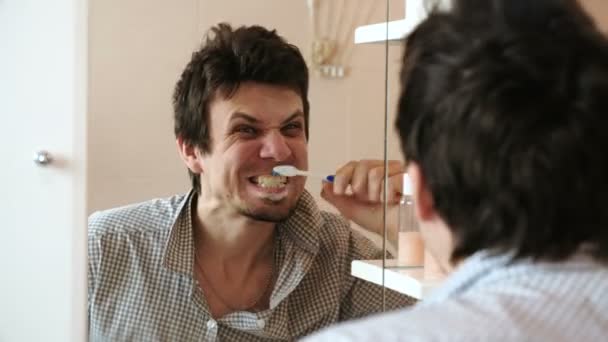 Crazy man poetst zijn tanden, kijkt naar zijn spiegelbeeld in de spiegel. — Stockvideo