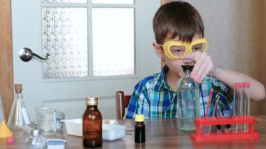 Evde kimya üzerinde deneyler. Çocuk bir şişe su alır ve bir pipet ile tüp içine su dökülen. Önden Görünüm.