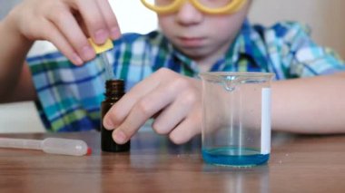 Evde kimya üzerinde deneyler. Çocuk bir kavanoz mavi sıvıyı içine bir ölçek bir pipet ile dökülen.