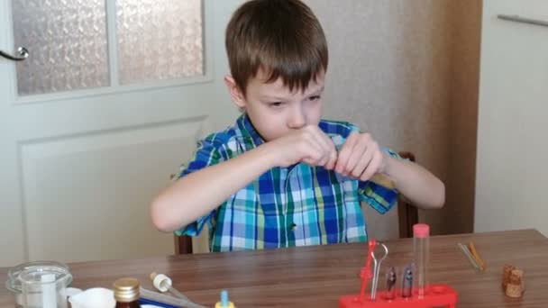 Experimenty na chemii doma. Chlapec v kostkované košili sedí u stolu a čistí trubice s kartáčem. — Stock video