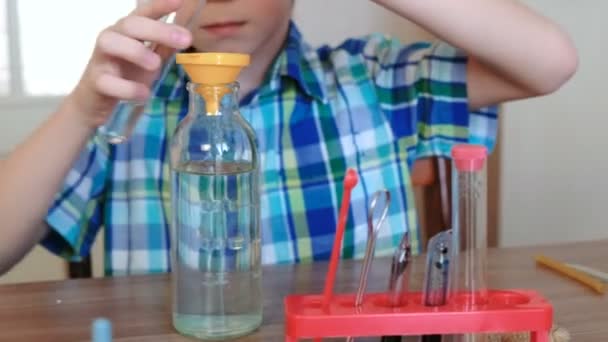 Experimente zur Chemie zu Hause. Nahaufnahme der Jungenhände, die Wasser aus dem Schlauch durch den Trichter in die Flasche schütteten. — Stockvideo