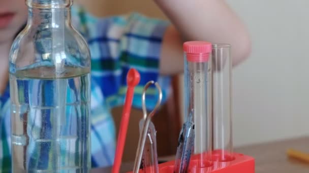 Эксперименты по химии дома. Мальчики крупным планом наливают воду из бутылки в трубку с помощью пипетки. Вид спереди . — стоковое видео