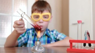 Evde kimya üzerinde deneyler. Çocuk tüp üzerinde alkol lamba yanan kırmızı sıvı ile ısıtır. Sıvı kaynar.
